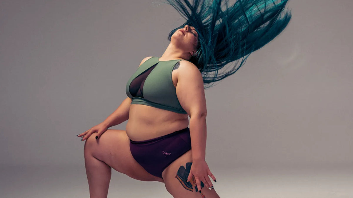 Danseuse à genou en brassière vert sauge à empiècements en mesh et short de pole dance prune, les cheveux en mouvement